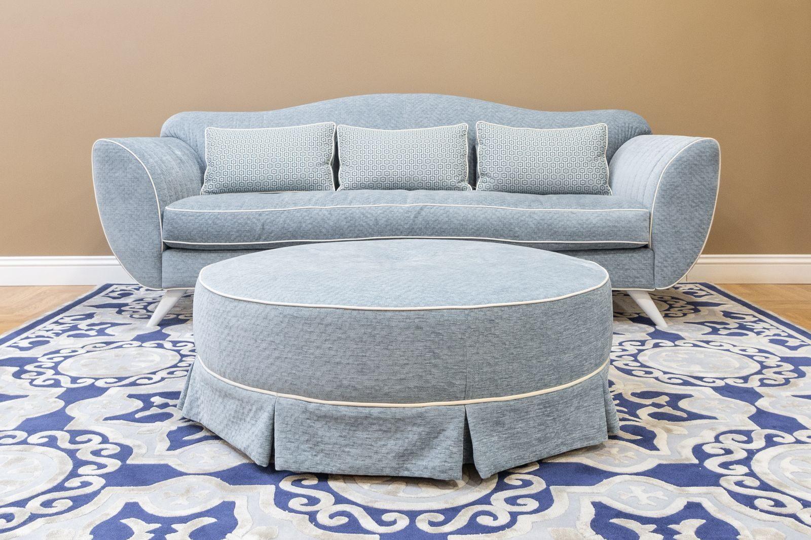 A stylish blue sofa with matching ottoman and decorative rug in a modern living room setting.